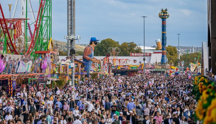 Festplatz voller Menschen bei Tag. Im Hintergrund Fahrgeschäfte und die Fruchtsäule.