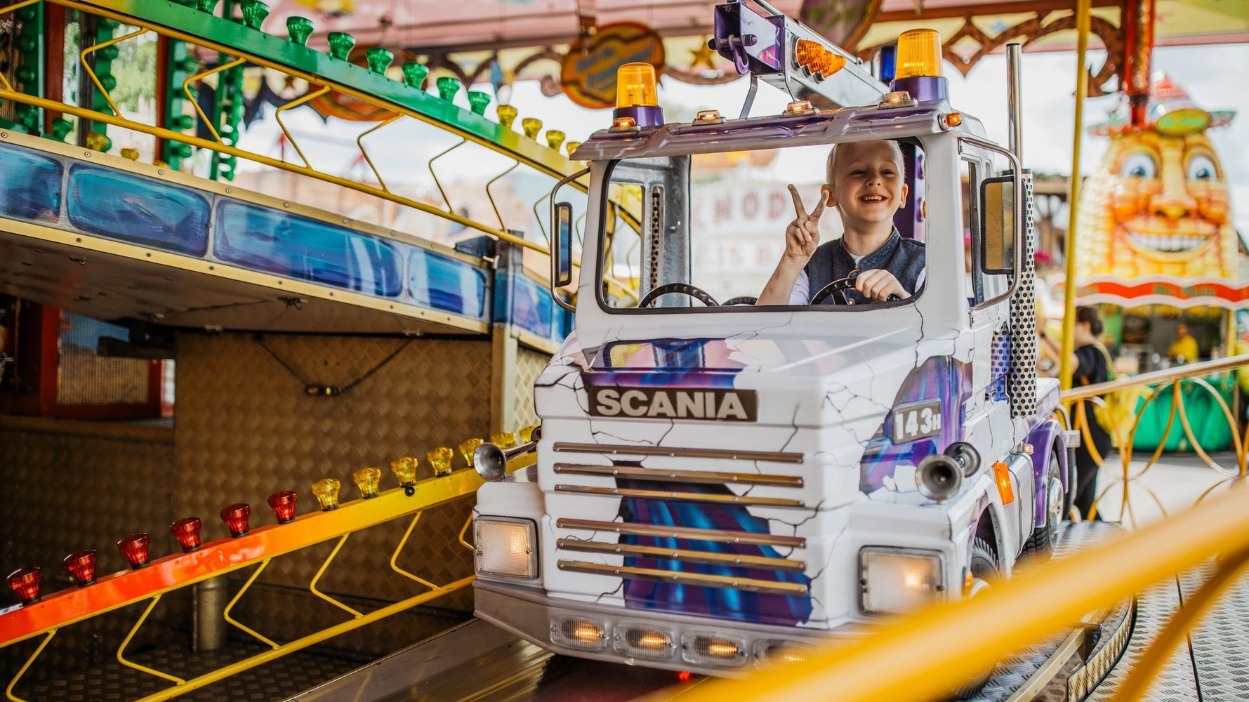 Junge sitzt in einer Kinderschleife in einem LKW und zeigt mit den Fingern das Peace-Zeichen in die Kamera.