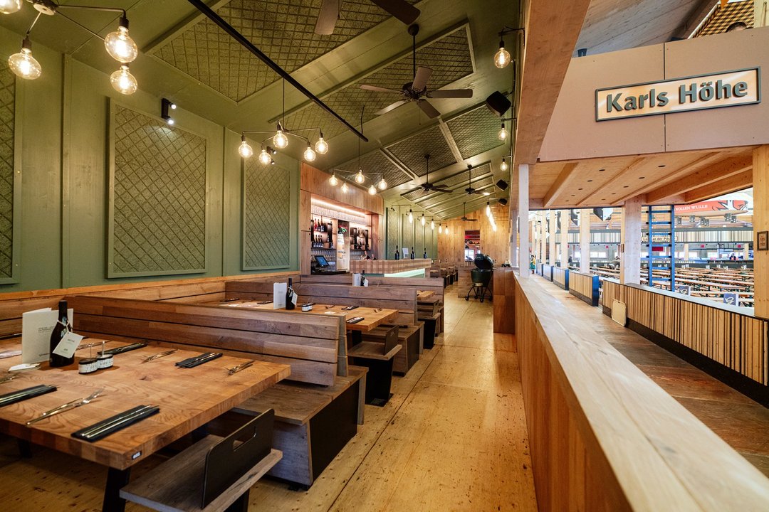 Die Karls Höhe im Göckelesmaier-Festzelt - ein gesonderter Sitzbereich mit Holztischen und Bänkenm dahinter ist direkt eine Bar.