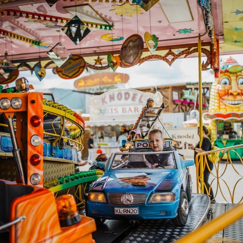 Ein Kind sitzt strahlend in einem Polizeiauto eines Kinderkarussells und lächelt in die Kamera