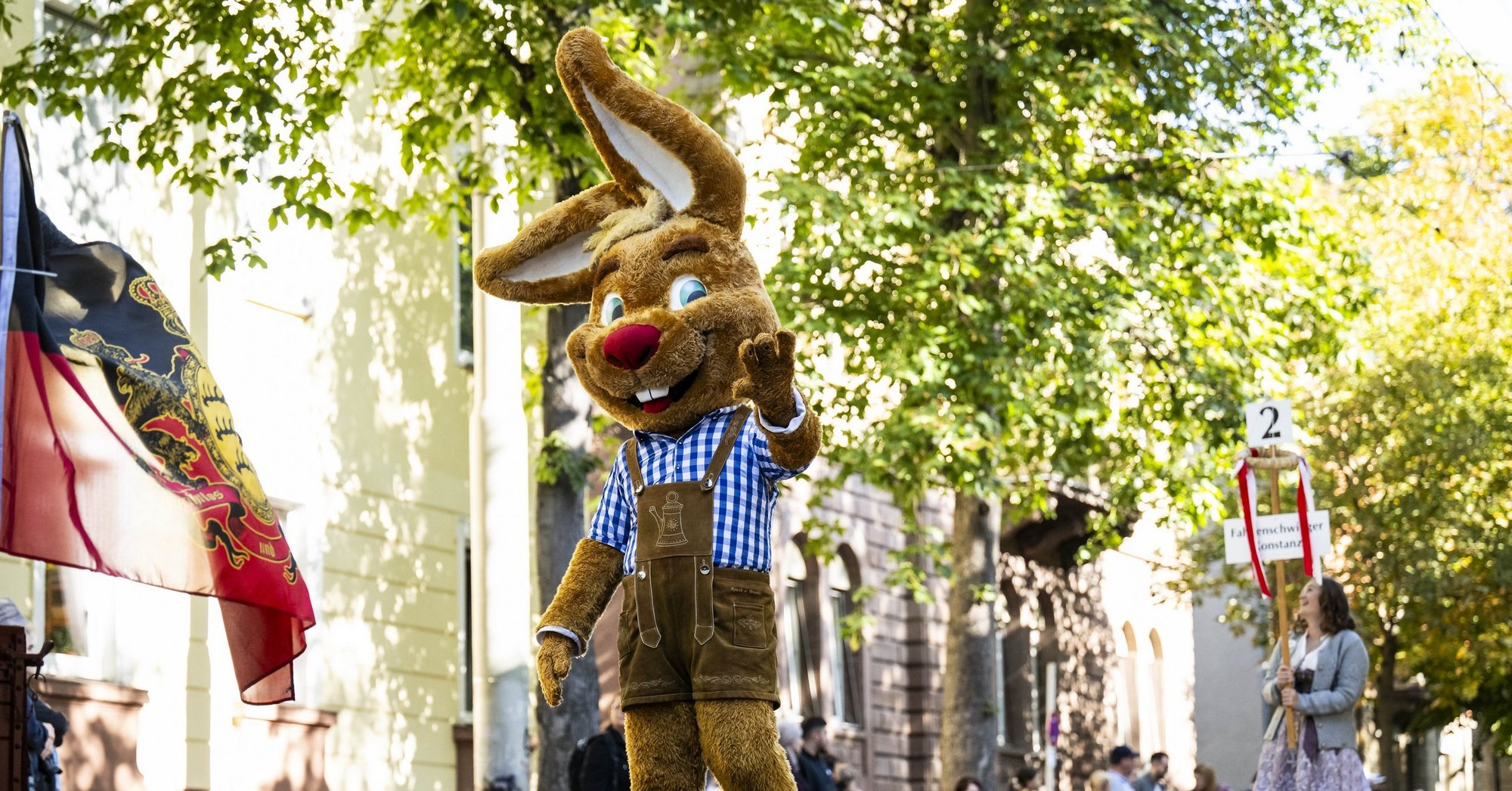 Das Maskottchen "Wasi" läuft beim Volksfest-Umzug durch Bad Cannstatt und winkt.