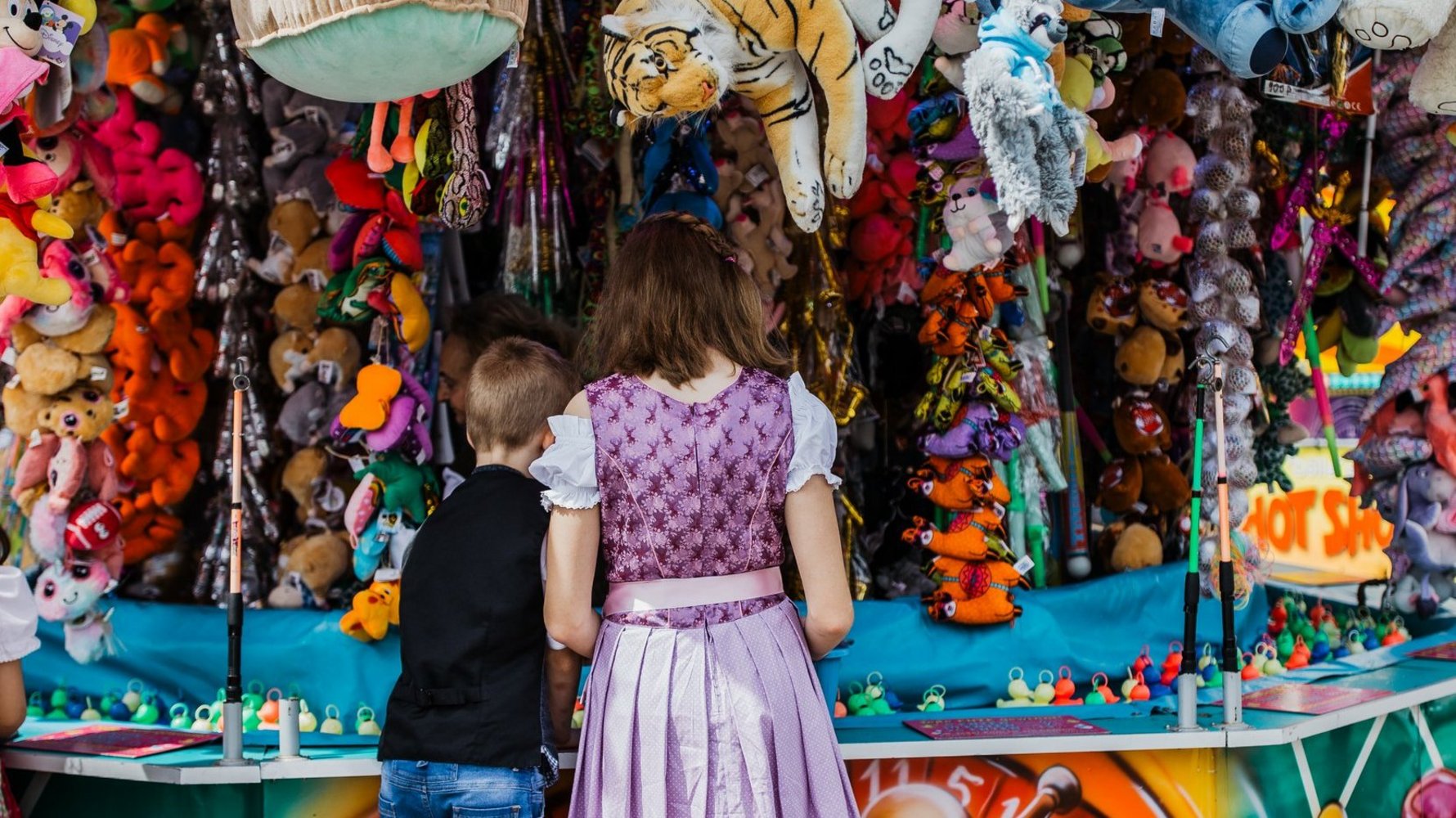 Ein Junge und ein Mädchen in Tracht stehen an einem Enten-angeln-Stand und versuchen ihr Glück