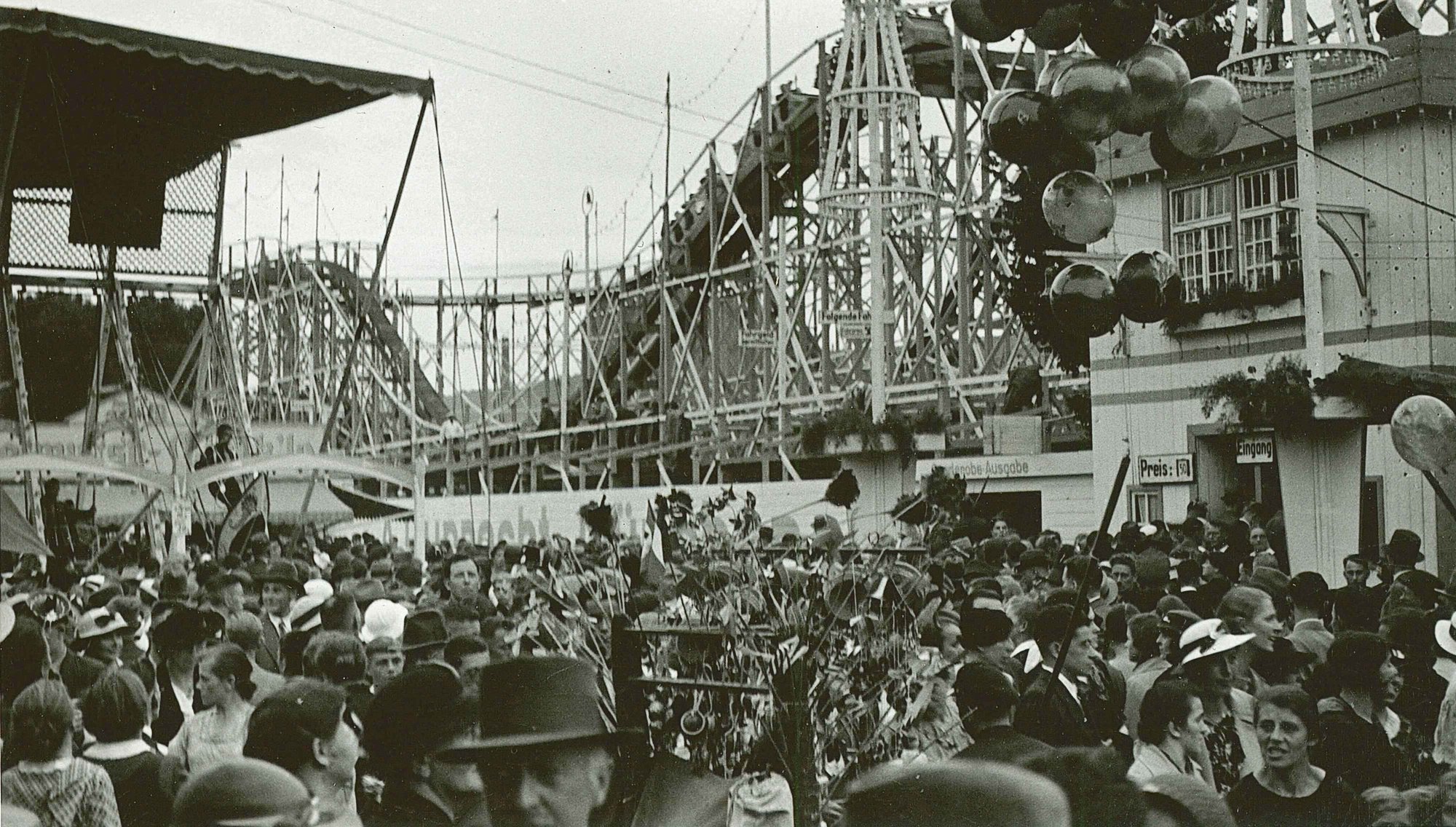 Schwarz-Weiß-Foto vom Volksfest Mitte der 1930er-Jahre mit einer Achterbahn im Hintergrund.