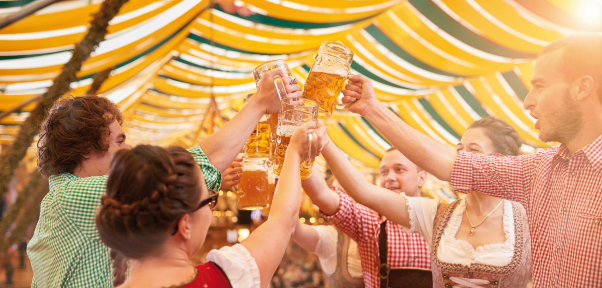 Men and women standing on a beer bench in a Fetzelt and clinking beer mugs together. 