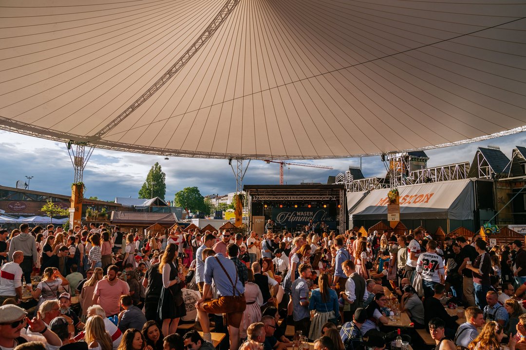 Viele Menschen stehen und sitzen unter dem Zeltdach des Wasenhimmels im Albdorf und feiern.