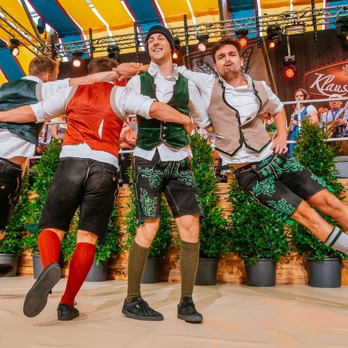 Drei Männer führen einen traditionellen Tanz in einem Festzelt auf.