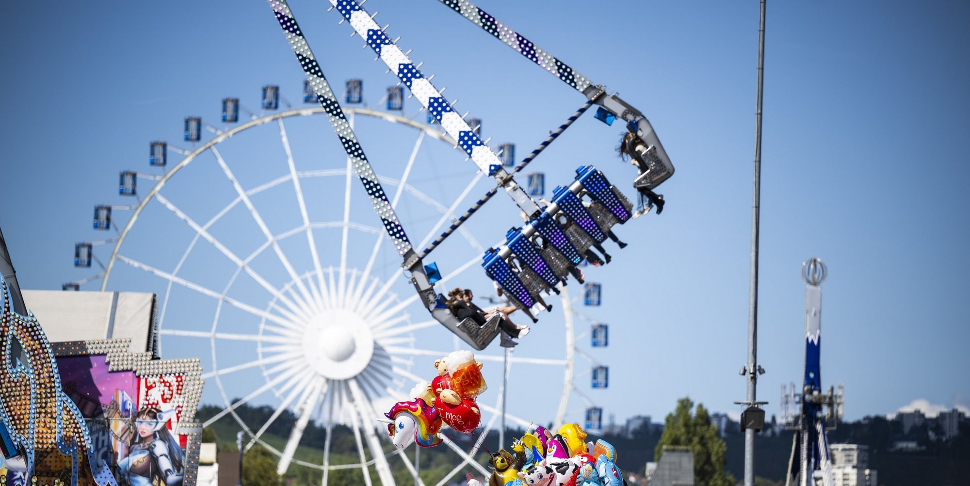 Ein Fahrgeschäft startet gerade mit Passagieren an Board. Im Hintergrund sieht man das Riesenrad.