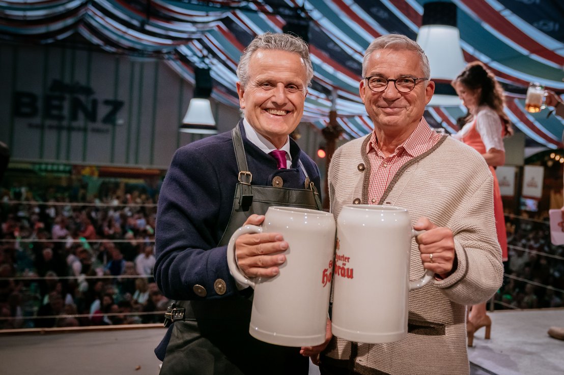 Stuttgarts Oberbürgermeister Frank Nopper und Innenminister Thomas Strobl stoßen nach dem Fassanstich im Festzelt "Beim Benz" mit ihren Ton-Maßkrügen an und blicken freudig in die Kamera