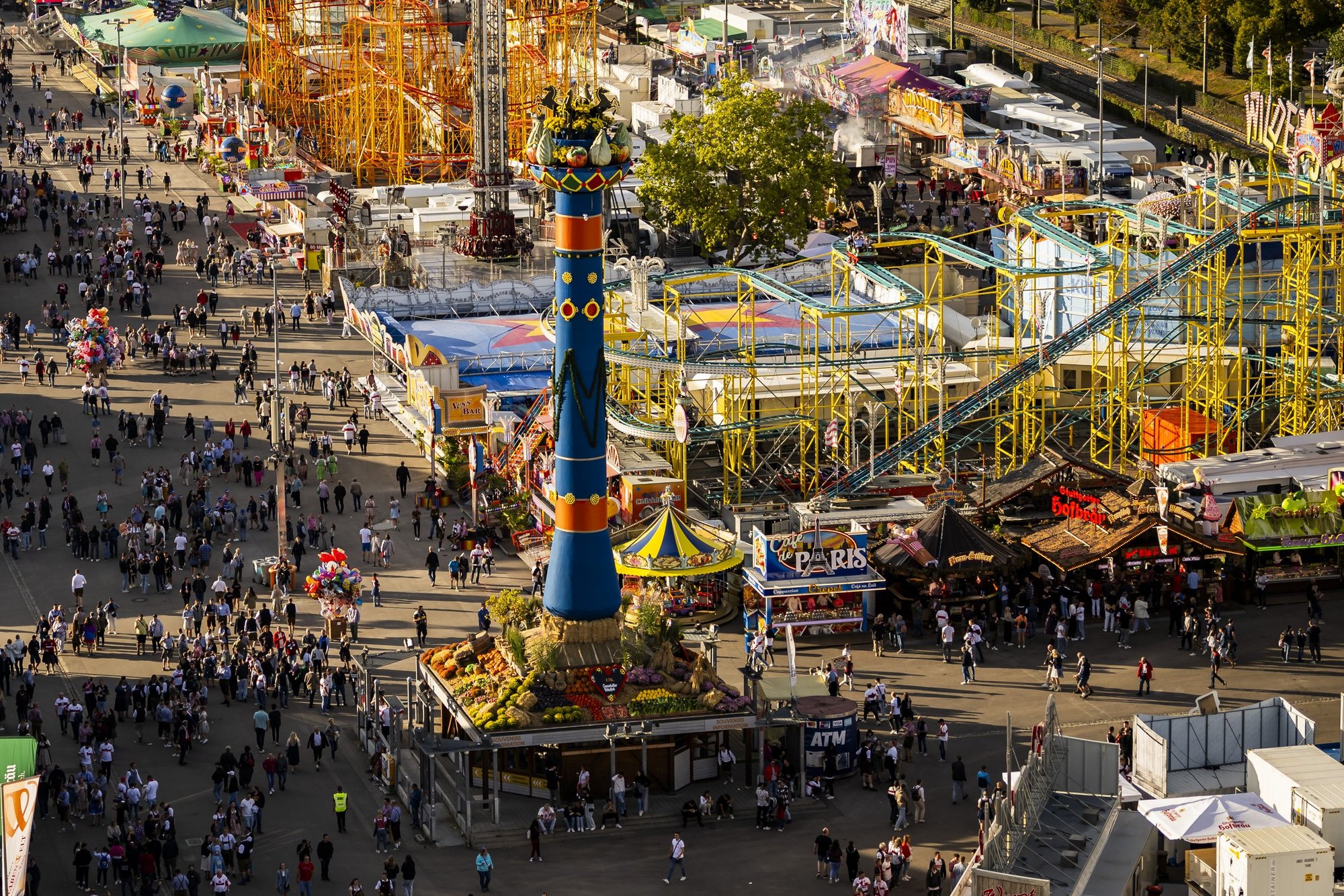 Vogelperspektive auf das Treiben auf dem Wasen. Unzählige Menschen laufen an der Fruchtsäule vorbei. Drumherum stehen Fahrgeschäfte.