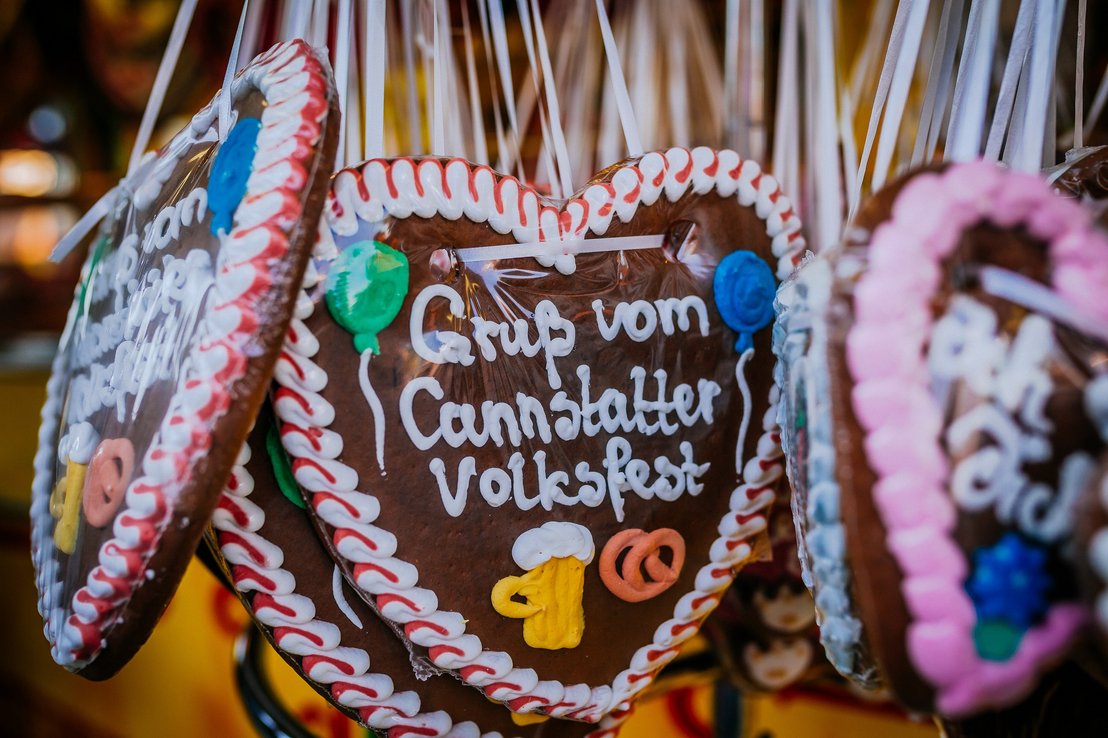Verschiedene Lebkuchenherzen, die an einer Stange hängen. Darauf steht unter anderem "Gruß vom Cannstatter Volksfest"