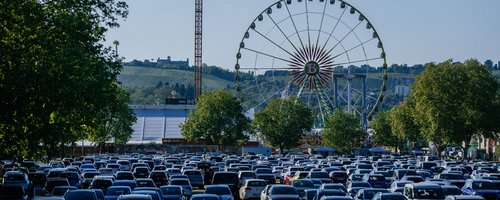 Blick vom Parkplatz P10 auf den Wasen. Im Vordergrund stehen viele Autos, im Hintergrund steht das Riesenrad und das Fahrgeschäft Aeronaut.
