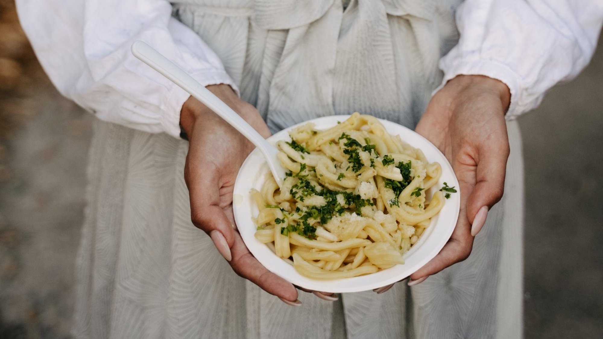 Eine Frau in einem grauen Dirndl hält einen Teller mit Schupfnudeln in die Kamera.