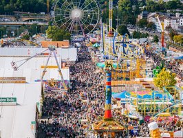 Vogelperspektive auf den Wasen. Links stehen die ganzen Bierzelte, in der Mitte thront die Fruchtsäule. Drumherum laufen tausende Menschen über den Platz.