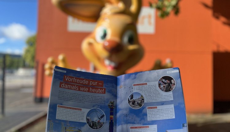 Das neue Live-Magazin Ausgabe Herbst 2025 aufgeschlagen beim Artikel zum Volksfest. Im Hintergrund steht eine große Wasen-Hasi-Figur.