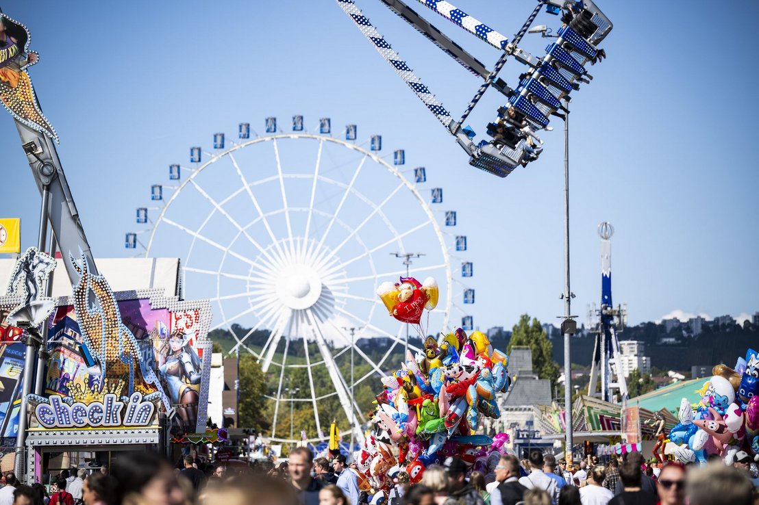 Blick über das Volksfest - ein Fahrgeschäft beginnt gerade seine Runde zu drehen. Im Hintergrund sieht man das Riesenrad.
