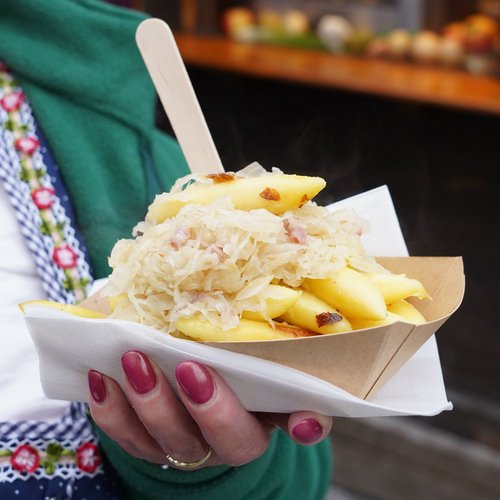 Eine Frau hält Schupfnudeln mit Sauerkraut in ihrer Hand. Oben steckt eine Holzgabel im Essen