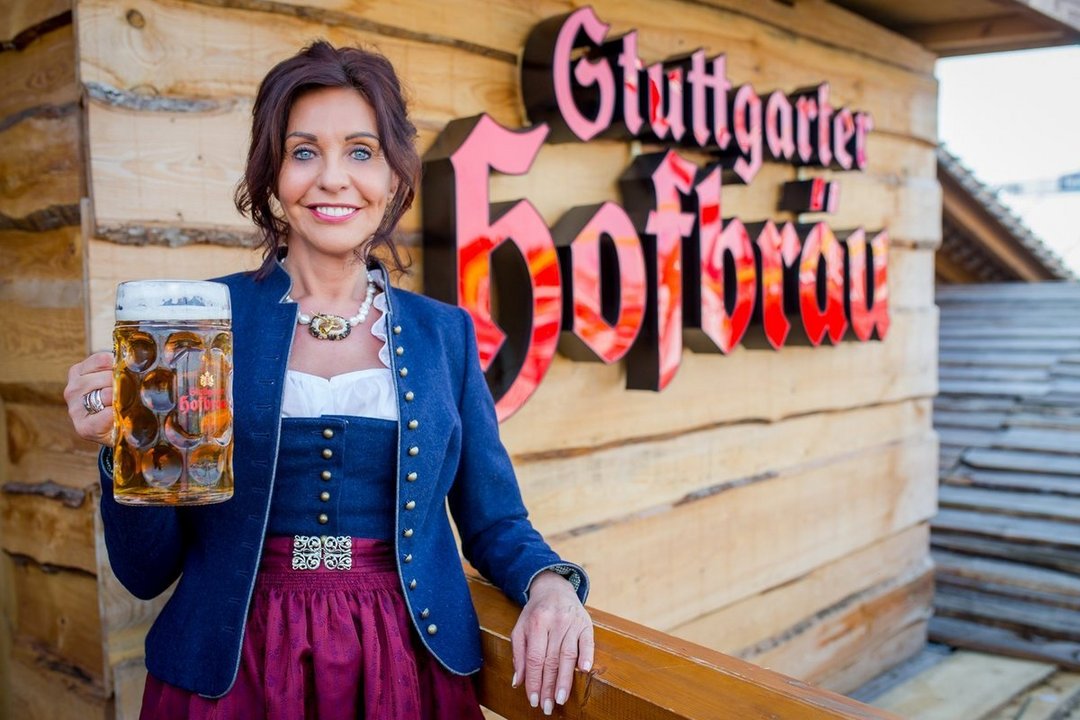 Sonja März steht mit einem Maßkrug vor einem Logo von Stuttgarter Hofbräu