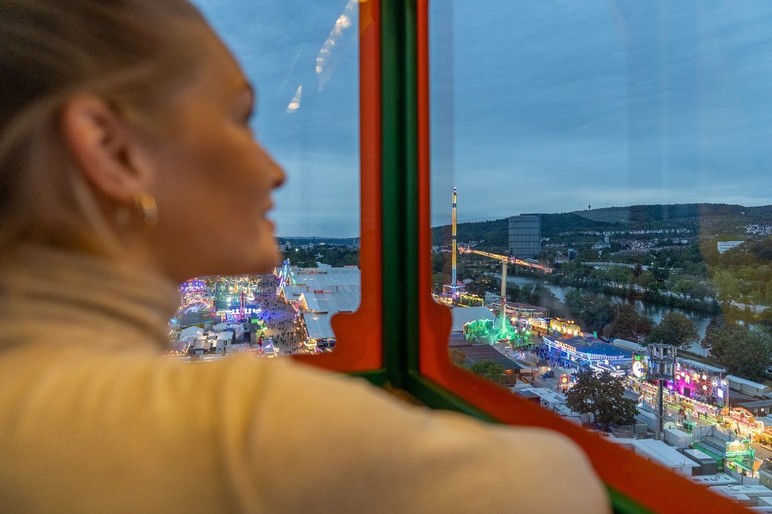 Frau im Riesenrad mit Ausblick über den Wasen in der Dämmerung.