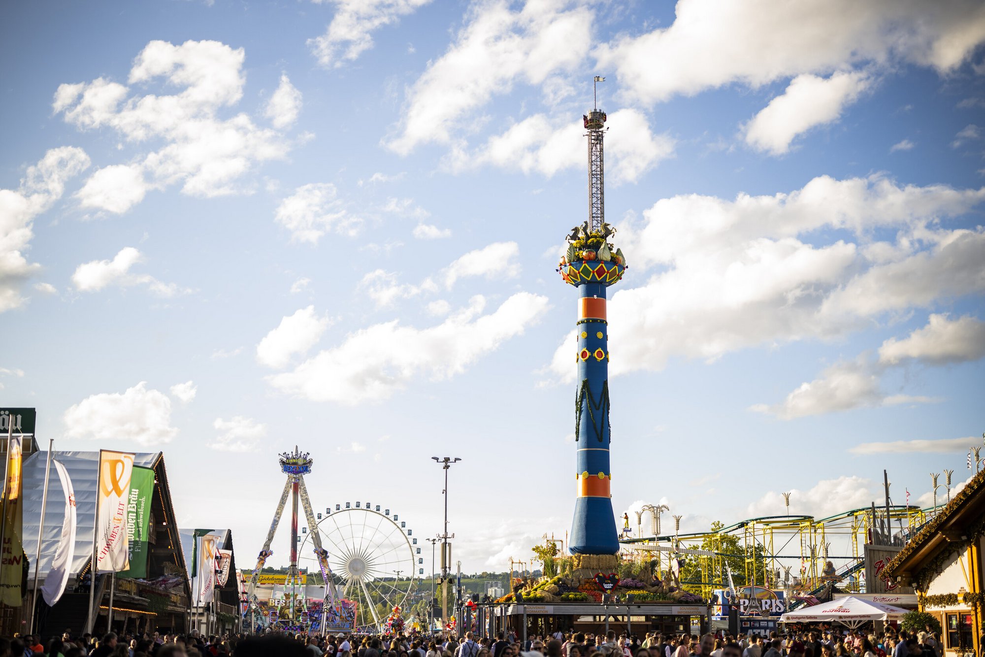 Blick über den Volksfestplatz mit der Fruchtsäule auf der rechten Seite. Links stehen die Bierzelte. Im Hintergrund sieht man Fahrgeschäfte.