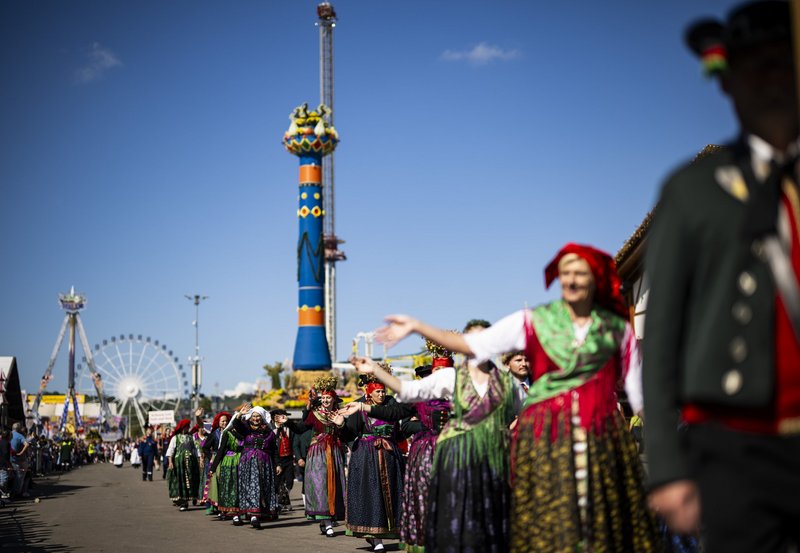 Traditionell gekleidete Menschen ziehen beim Volksfestumzug über den Wasen. Im Hintergrund steht die Fruchtsäule