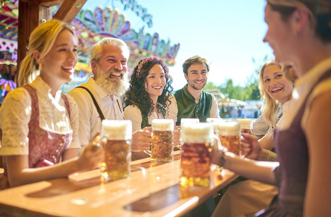 Sieben Personen sitzen im freien aun einem Biertisch mit jeweils einem Bier in der Hand und unterhalten sich gesellig.