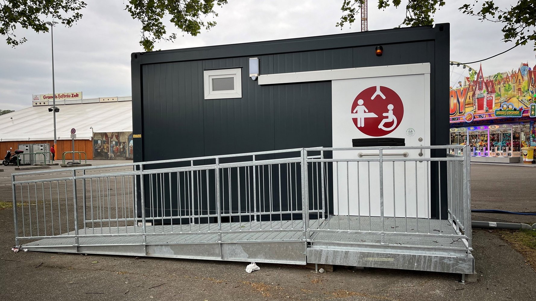 Ein grauer Container mit weißer Tür, auf der das Logo der Toilette für alle klebt.