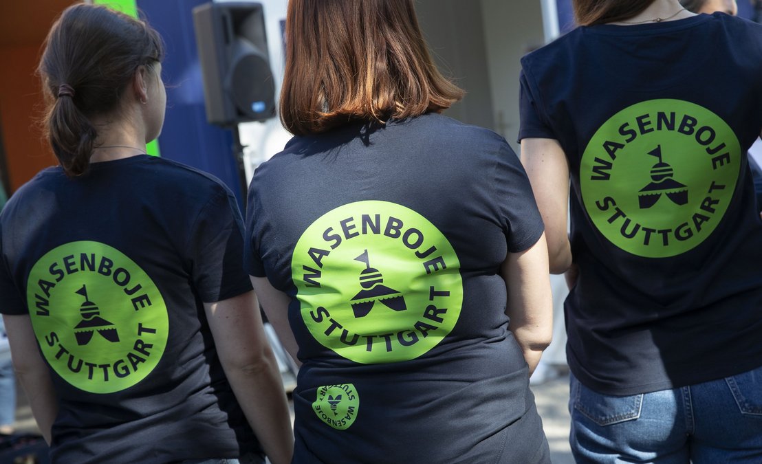 Drei Frauen stehen mit dem Rücken zum Fotografen und haben alle das gleiche T-Shirt an. Ein dunkelblaues Shirt mit einem grünen Logo der Wasenboje Stuttgart