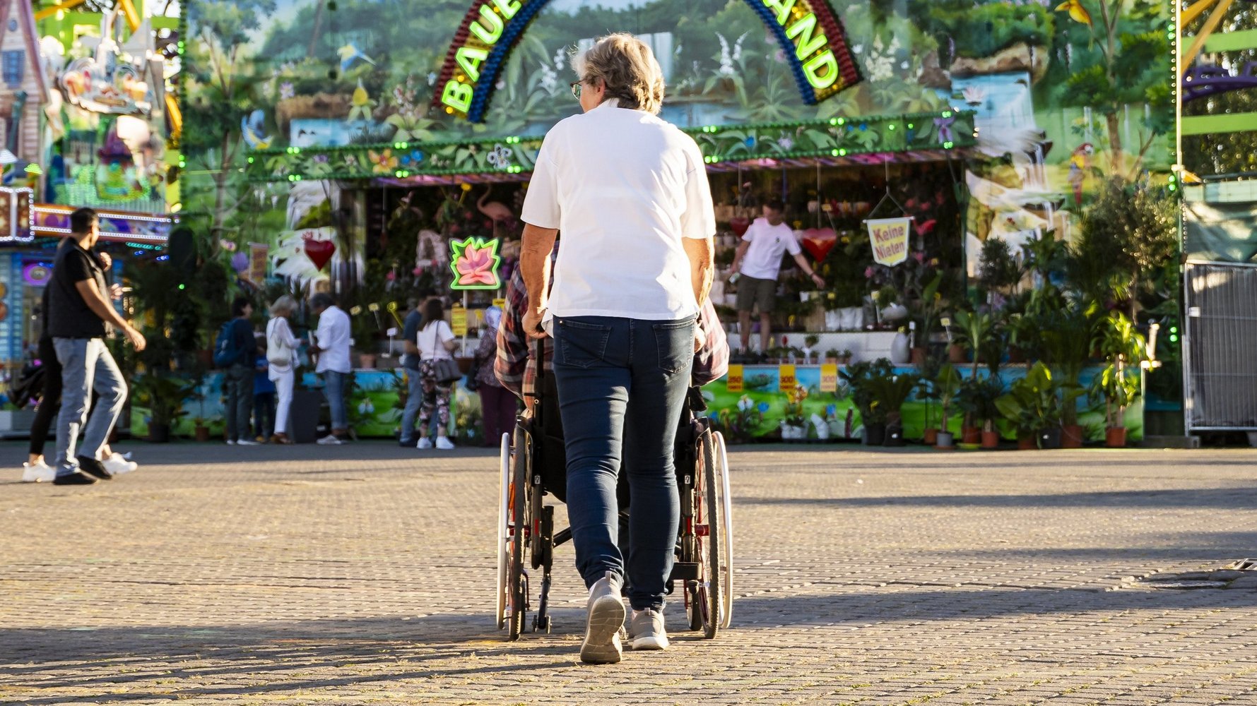 Eine Frau schiebt eine Person im Rollstuhl über den Festplatz.