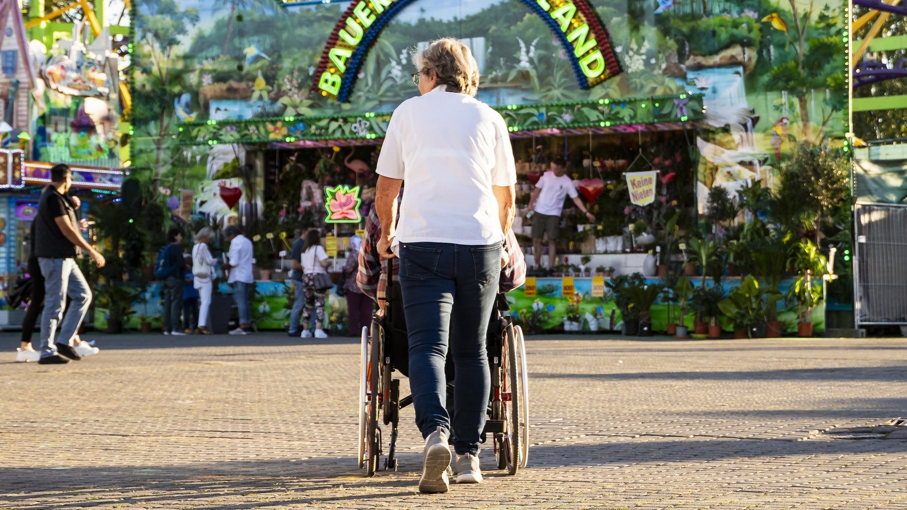 Eine Frau schiebt eine Person im Rollstuhl über den Festplatz.