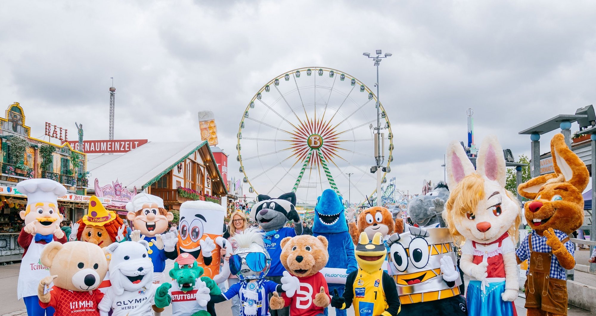 Zahlreiche Maskottchen stehen zum Gruppenfoto nebeneinander. Im Hintergrund sieht man das Riesenrad.