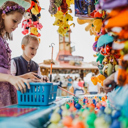 Ein Junge und ein Mädchen in Tracht versuchen ihr Glück beim Entenangeln.