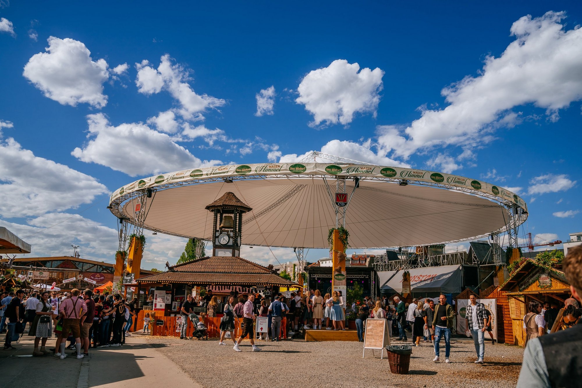 Ein großer weißer Schirm im Albdorf, der sogenannte Wasenhimmel. Darunter sitzen Menschen auf Bierbänken und trinken und essen und feiern.