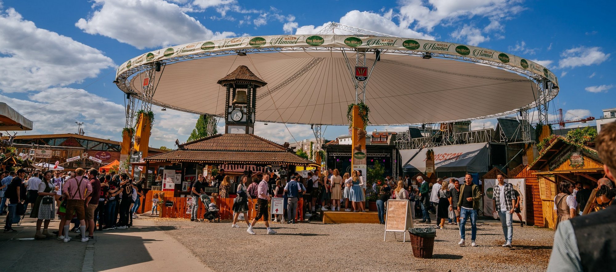 Ein großer weißer Schirm im Albdorf, der sogenannte Wasenhimmel. Darunter sitzen Menschen auf Bierbänken und trinken und essen und feiern.